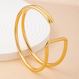 Close-up of polished gold double-layered open bangle on a white textured stone base