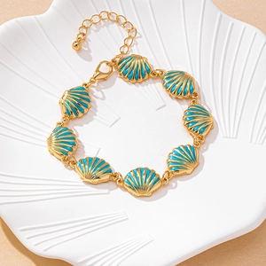 Detail view of ocean-style gold chain bracelet with blue shell charms and heart pendant