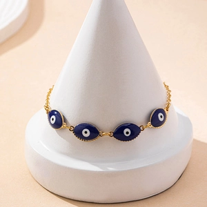 Gold evil eye bracelet with blue oval charms on a minimalist white jewelry stand