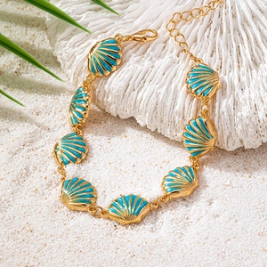 Gold-tone bracelet with light blue enamel shell charms on a summer beach sand background
