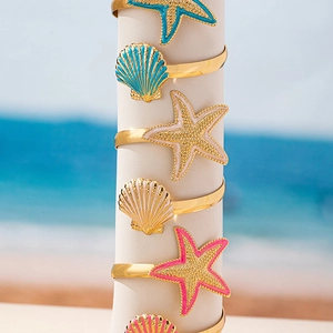 Colorful starfish and seashell bracelets on gold rings with a sunny beach background