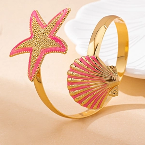 Detail of gold starfish and seashell bracelet with pink enamel on a white shell tray