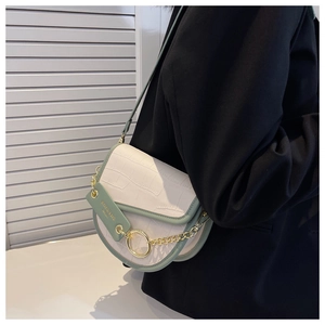 Detail of white crocodile embossed saddle bag with green trim and gold chain accents