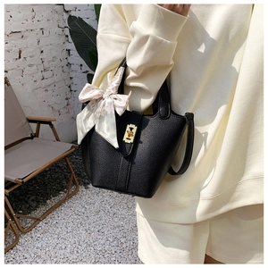 Dettaglio borsa a secchiello in pelle nera con chiusura dorata e foulard decorativo in seta