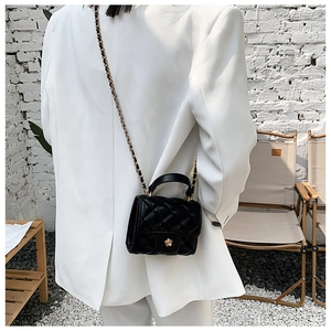 Detail of black quilted mini cloud bag with golden flower buckle and chain strap