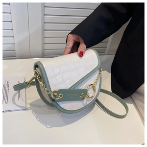 Detail of cream crocodile texture saddle bag with green trim and gold chain strap