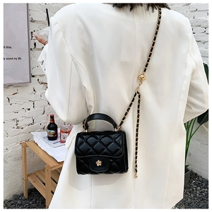 Detail of black quilted mini bag with gold flower clasp and chain strap on white blazer