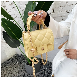 Detail of light yellow quilted bag with camellia metal lock and gold chain strap