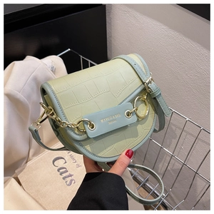 Detail of light green crocodile embossed saddle bag with gold ring and chain link