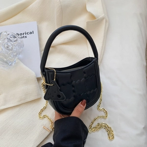 Chic black quilted biscuit bag with gold chain and cheese pendant in a minimalist setting