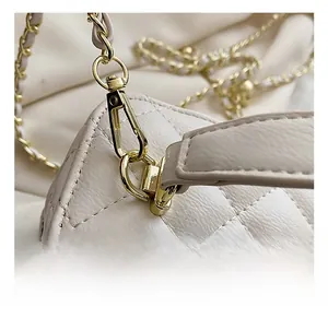 Macro view of light gold lobster clasp and woven chain strap on white quilted bag