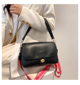 Détail du sac bandoulière en cuir noir avec sangle rayée rouge sur un blazer blanc