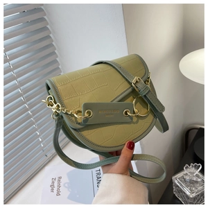 Detail of light green faux crocodile saddle bag with gold chain and leather tag