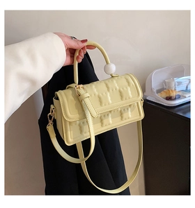 Détail d'un sac à main jaune avec motif gaufré et perle blanche décorative sur l'anse