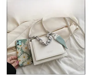 Close-up of beige crossbody flap bag with chain handle and scarf beside a phone case