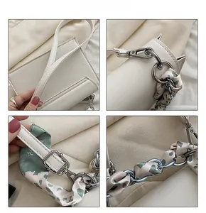 Detail of white crossbody bag featuring silver hardware and silk scarf chain handle