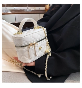 Detail of white quilted mini bag featuring golden bee ornament and adjustable chain strap