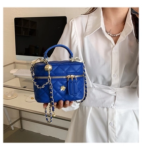 Detail of blue quilted mini bag with gold chain strap and floral accent on the handle