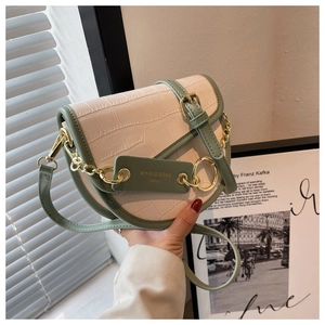 Detail of a contrast color saddle bag with crocodile texture and gold chain strap