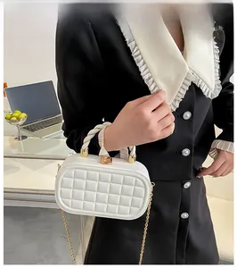 Close-up of white quilted box bag with golden metal clasp and woven chain strap details