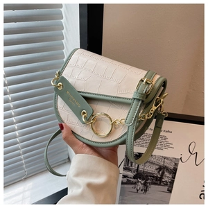 Detailed view of cream crocodile-embossed leather saddle bag with sage green trim and gold ring