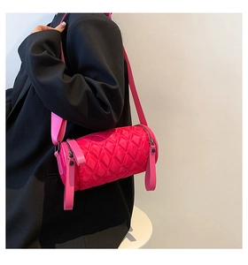 Side view of a bright pink quilted cylinder crossbody bag worn with a black suit