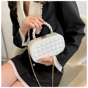 Close-up of a white quilted box bag with a gold twist lock and woven top handle
