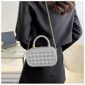 Detail of silver box bag featuring quilted texture and golden chain on a shoulder strap