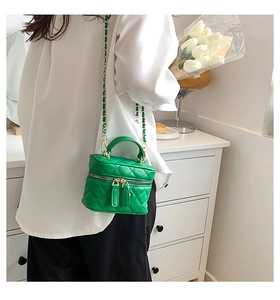 Detail of green quilted crossbody bag with gold chain strap worn with white shirt