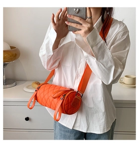 Detail of orange quilted nylon cylinder bag with wide strap in a casual lifestyle setting