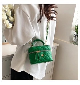 Detail of green quilted crossbody bag with gold chain strap and floral zipper pull charms