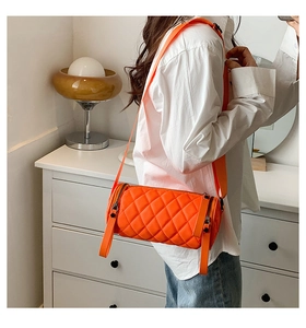 Close-up of bright orange quilted nylon cylinder bag with a wide crossbody strap on a model