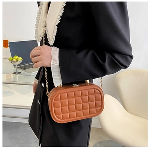 Detail of a brown quilted box bag with gold chain strap on a model with blazer