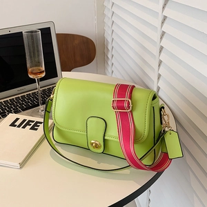Sac à main vert citron en cuir avec bandoulière rayée et fermoir rotatif doré sur table