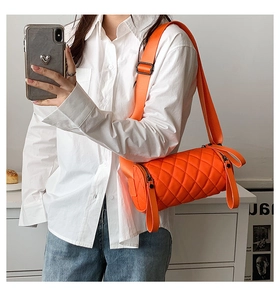 Close-up of bright orange quilted cylinder bag with adjustable wide nylon shoulder strap