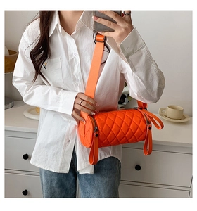 Detail view of orange quilted nylon cylinder bag with wide strap on a model
