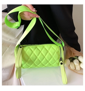 Detail of neon quilted cylinder bag featuring dual black zippers and wide strap nylon texture