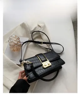 Detail of black crocodile texture handbag with gold square buckle and white chain accent