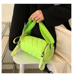 Quilted cylinder bag in neon green nylon fabric with wide strap shown on a black blazer