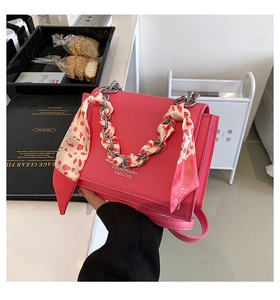 Close-up of pink leather crossbody bag with silver chain handle and floral scarf detail