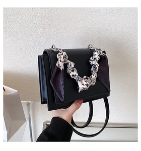Detail of black crossbody bag with silk scarf handle and silver chain ornament