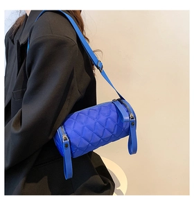 Detail of blue quilted nylon barrel bag featuring a wide shoulder strap worn by a model