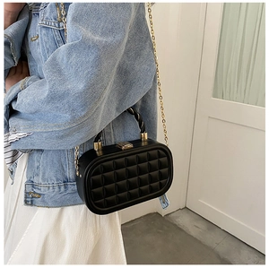 Detail of black quilted box bag with gold chain strap worn by a model in denim