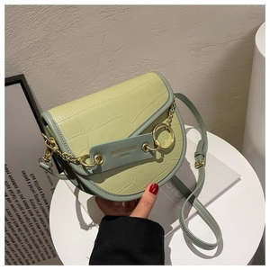 Macro detail of avocado green crocodile embossed saddle bag with gold chain and ring charm