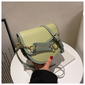 Detail of light green faux leather saddle bag featuring crocodile texture and gold chain