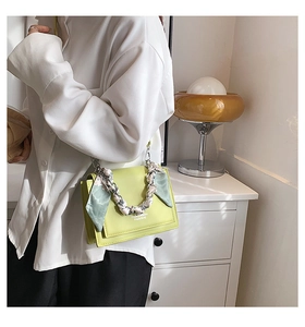 Detail of neon green crossbody bag with silk scarf wrapped around its metal chain handle