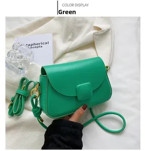 Détail d'un sac à rabat vert herbe avec dorures à côté d'un costume blanc
