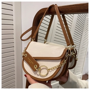 Detail of white crocodile texture saddle bag with brown trim and gold chain accents