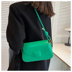 Gros plan d'un sac à bandoulière minimaliste vert en cuir porté par un mannequin