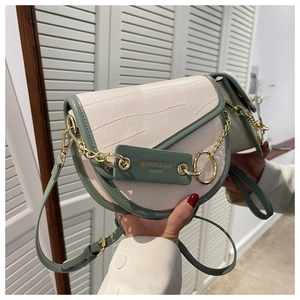 Detail of off-white crocodile embossed saddle bag with green trim and gold chain